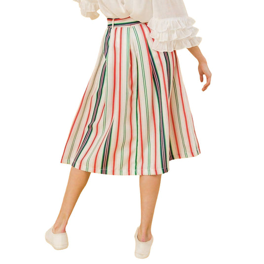 Close-up of the model walking, focusing on the pleated design and bold stripes of the midi skirt, emphasizing the pockets and the fluid movement of the fabric.