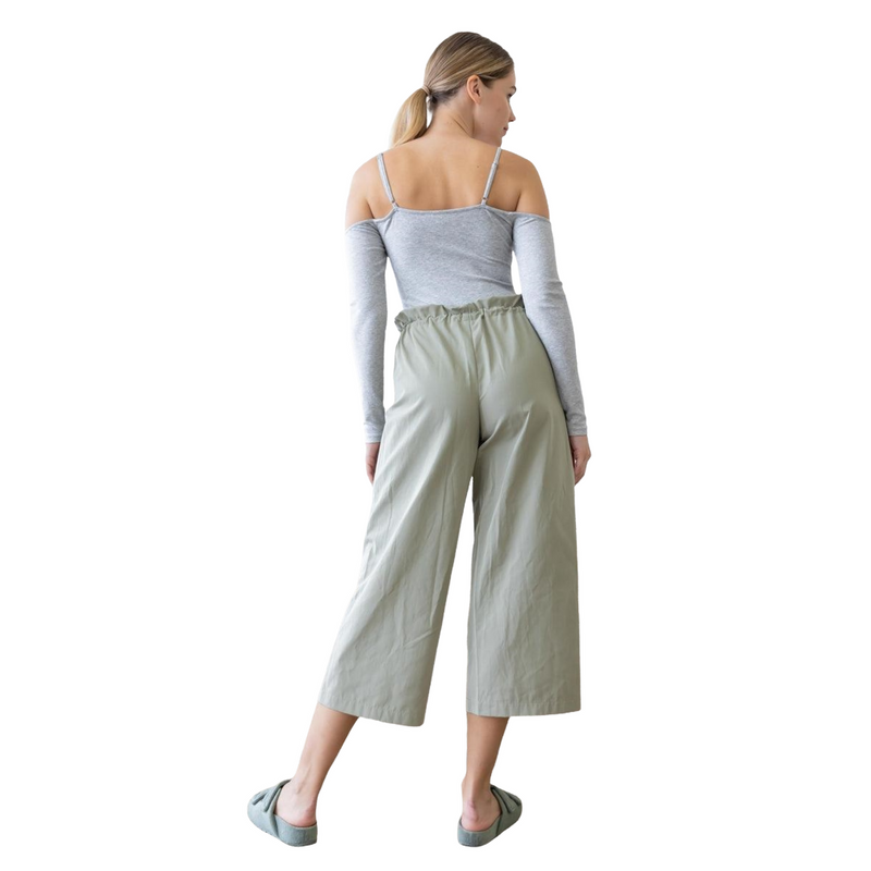 Load image into Gallery viewer, Back view of the Tasha Heather Grey Cold Shoulder Ribbed Bodysuit, worn by a model with high-waisted light green pants. The bodysuit&#39;s thin spaghetti straps and ribbed fabric create a comfortable and trendy look from all angles.
