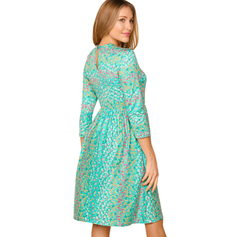 Load image into Gallery viewer, Back view of a woman in a teal floral dress with 3/4 sleeves, looking over her shoulder.
