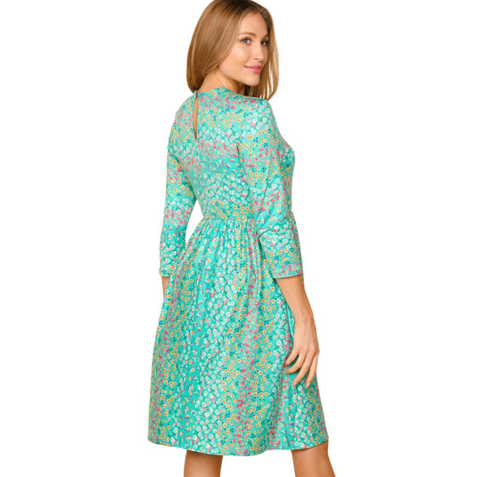 Back view of a woman in a teal floral dress with 3/4 sleeves, looking over her shoulder.