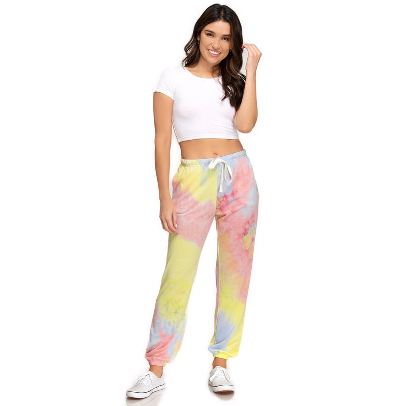 Load image into Gallery viewer, Smiling woman in vibrant yellow and pink tie-dyed jogger pants paired with a white cropped tee, standing against a plain background, showcasing the pants&#39; front view. The comfortable fit and lively colors make a casual yet chic statement.
