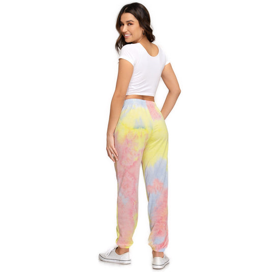 Rear view of a woman wearing yellow and pink tie-dyed jogger pants, complemented by a white cropped tee. She is looking over her shoulder, highlighting the pants' fit and the soft terry material, perfect for a relaxed style.