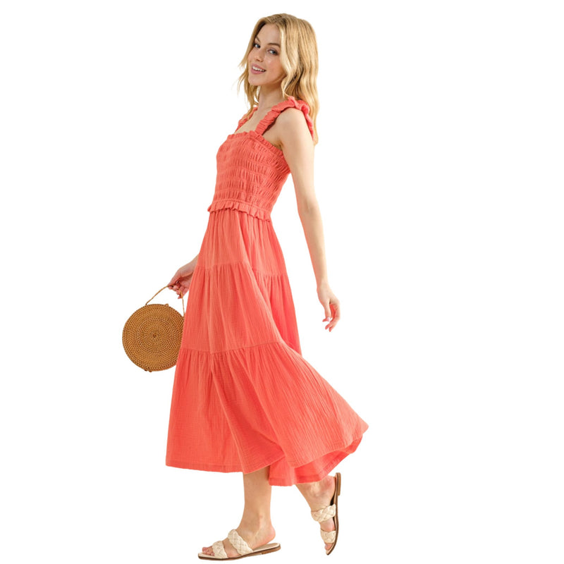 Load image into Gallery viewer, Woman wearing a coral Smocked Ruffled Tiered Dress, smiling and holding a woven handbag, showcasing the dress&#39;s flowy and lightweight design.
