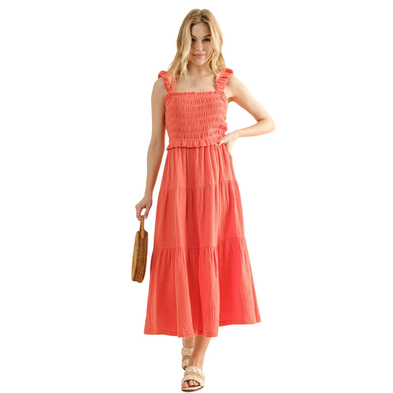 Load image into Gallery viewer, Front view of a woman in a coral Smocked Ruffled Tiered Dress, standing confidently and holding a woven handbag, highlighting the smocked bodice and ruffled tiers.
