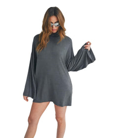 Woman in a gray turtleneck bell sleeve mini dress standing against a white background, posing with her right hand on her hip.
