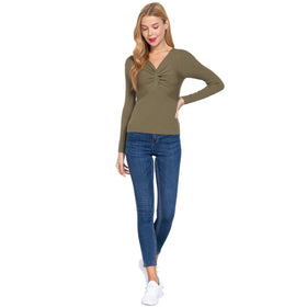 Full-length view of a woman wearing an olive green V-neck ribbed sweater featuring a unique twisted front detail, complemented by slim-fit blue denim jeans and white sneakers.