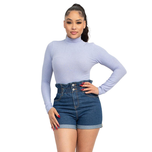 Confident woman posing in a light blue mock neck top and high-waisted denim shorts, exemplifying a casual yet chic ensemble.