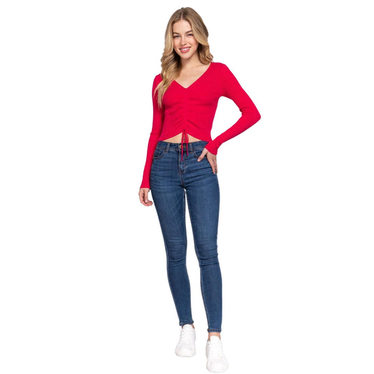 Full-body shot of a model sporting a fuchsia V-neck sweater with distinctive shirring at the waist, paired with form-fitting blue jeans.