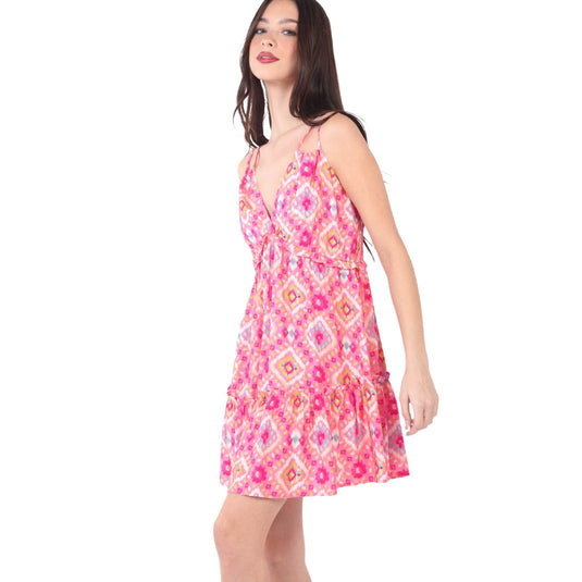 Side view of a young woman in a vibrant multi-color printed mini dress with a deep V-neckline and ruffled hem. The dress has thin shoulder straps and an open back, highlighting its stylish and playful look.