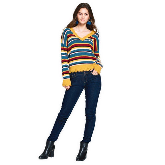 A woman models a vibrant striped V-neck sweater with yellow scalloped trim, paired with dark jeans and black ankle boots.