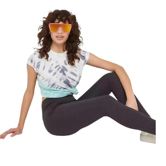 Casual style snapshot of a woman in charcoal gray high-waisted leggings and a tie-front cropped white t-shirt with a tie-dye design, completed with white sneakers and orange-tinted sunglasses.
